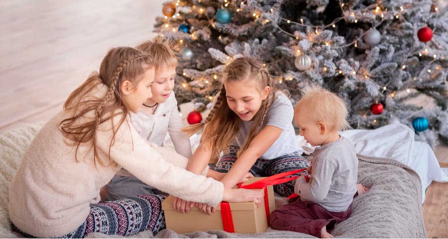 Siblings opening a gift in the living room next to a Christmas tree.